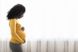 A pregnant woman holding her belly before her OB/GYN appointment to discuss her high-risk pregnancy.